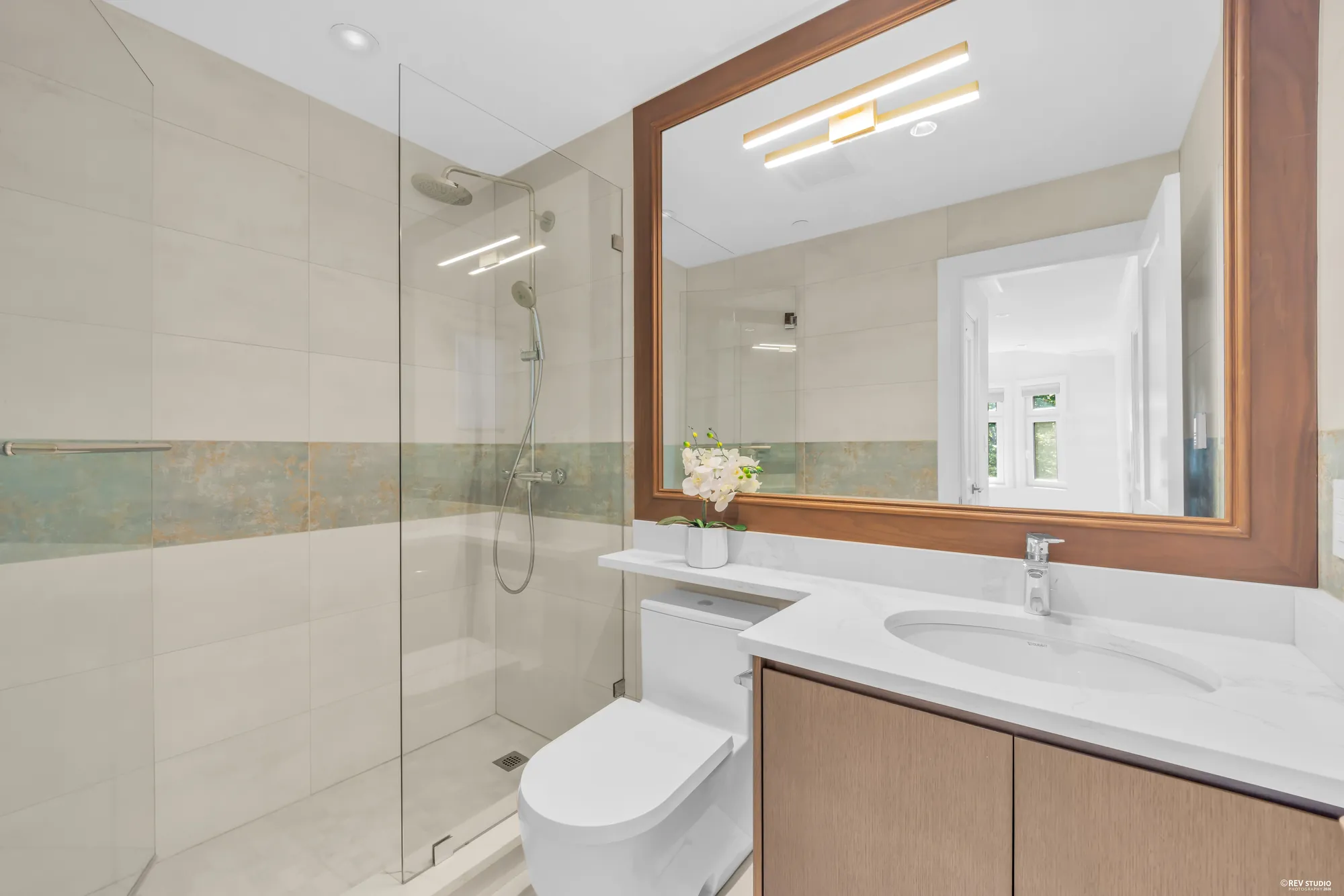 An upper-floor bathroom with a glass shower and a wood-framed mirror
