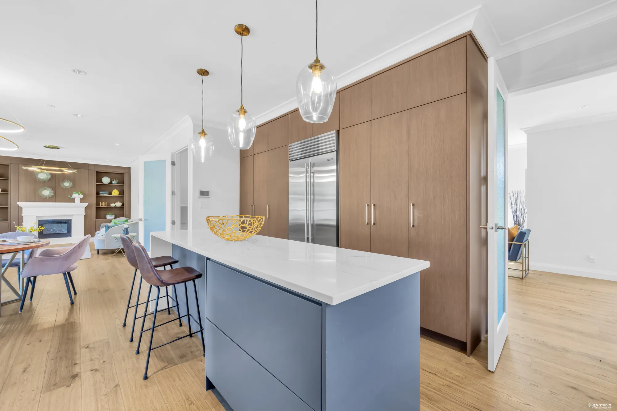 The kitchen island with bar stools, the tall oak cabinet wall behind