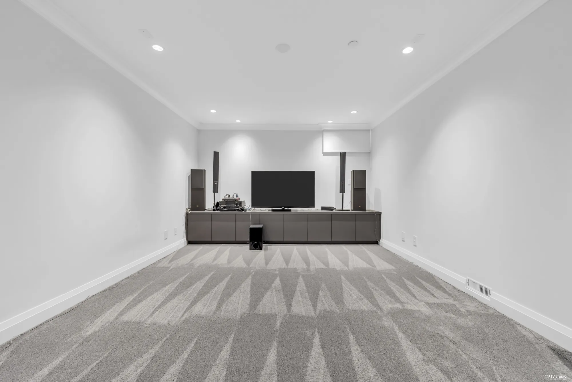 The theatre room, carpeted, with a screen and speakers along the end wall